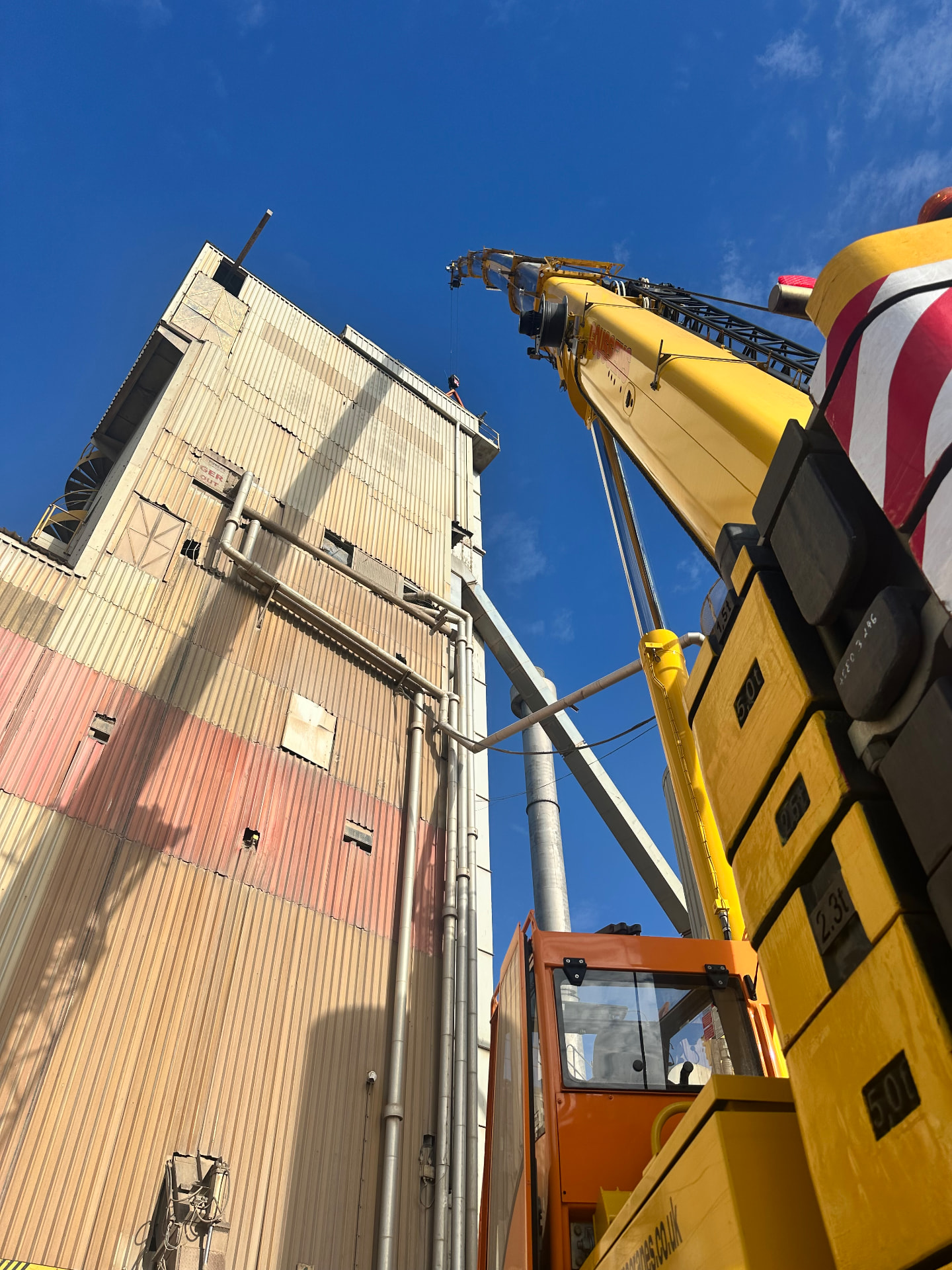 Mobile crane boom raised alongside an industrial silo building
